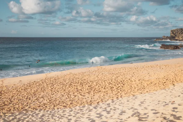 Plage de sable fin avec vagues turquoise et ciel nuageux