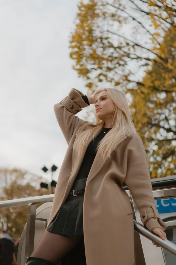 Jeune femme élégante en manteau beige dans un décor urbain automnal