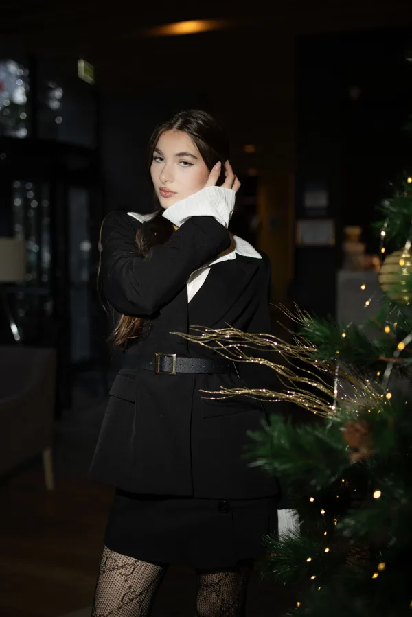 Jeune femme élégante en tenue noire près d’un sapin de Noël dans une ambiance festive