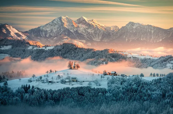 Village enneigé au lever du soleil devant les montagnes slovènes