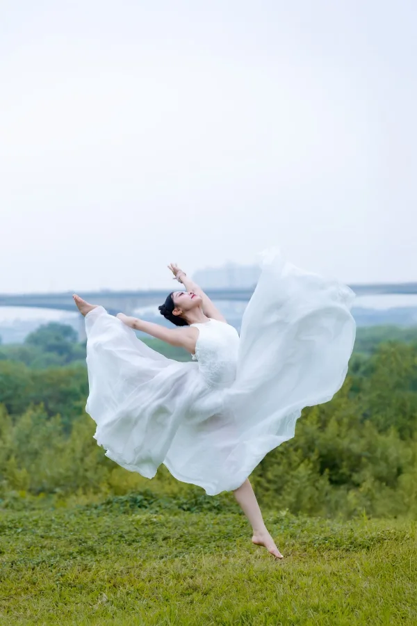 Danseuse en robe blanche réalisant un saut gracieux en plein air