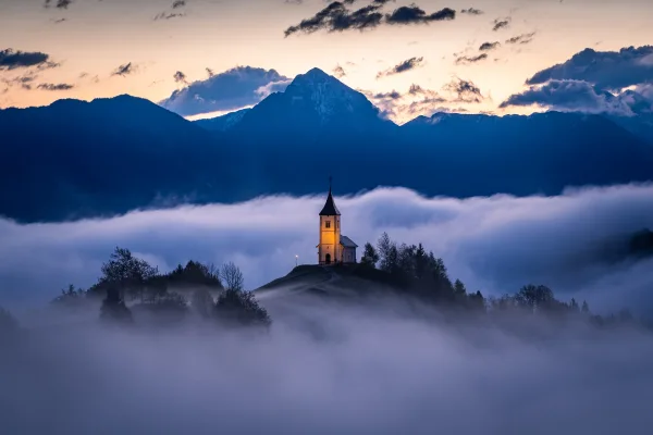 Église illuminée au sommet d’une colline dans la brume au coucher du soleil