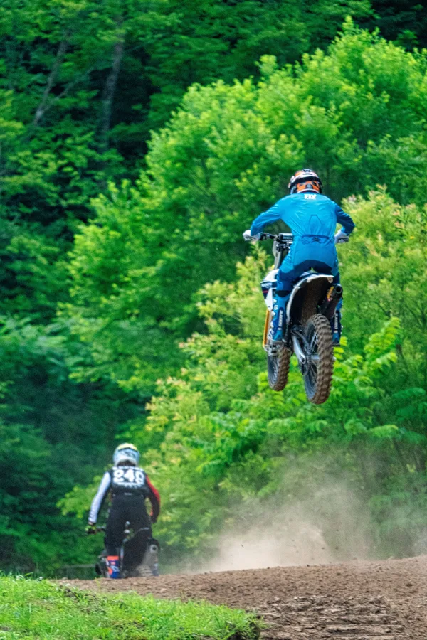 Pilote de motocross en plein saut sur une piste de terre en forêt