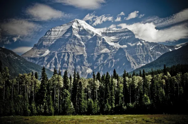 Montagne majestueuse entourée d'une forêt de conifères sous un ciel spectaculaire