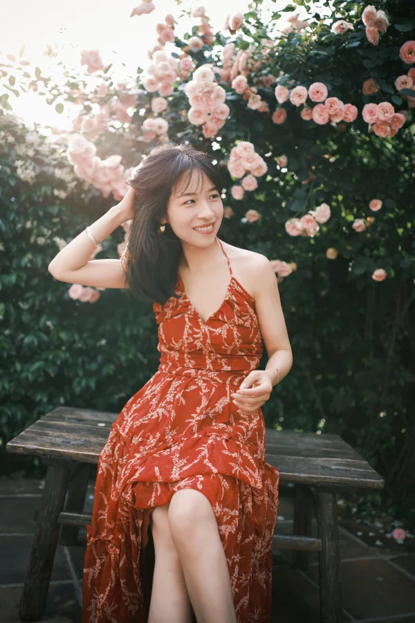 Jeune femme souriante en robe rouge dans un jardin fleuri de roses