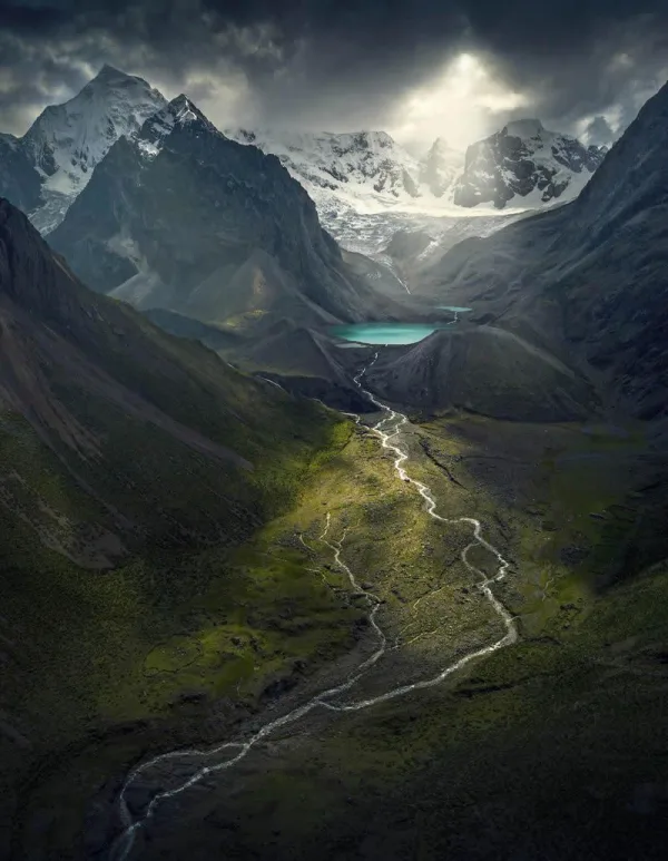 Vallée glaciaire avec rivière et montagnes enneigées sous un ciel orageux
