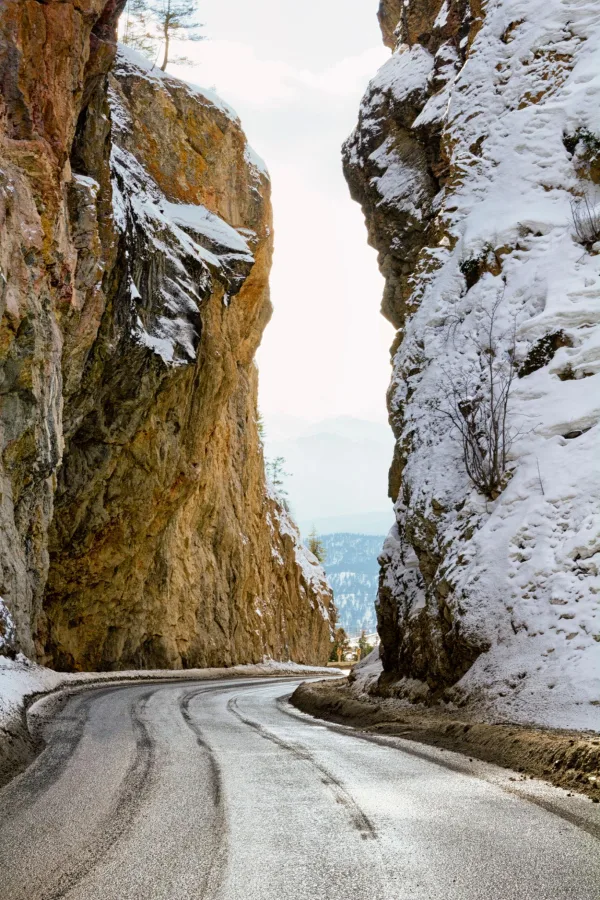 Route de montagne enneigée traversant un canyon rocheux en hiver