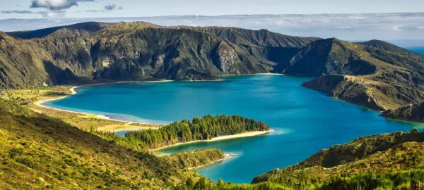 Lac volcanique aux eaux turquoise avec îlot boisé au cœur d'un paysage montagneux