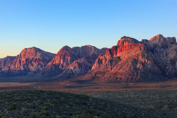 Montagnes rocheuses rouges illuminées au coucher du soleil dans un paysage désertique