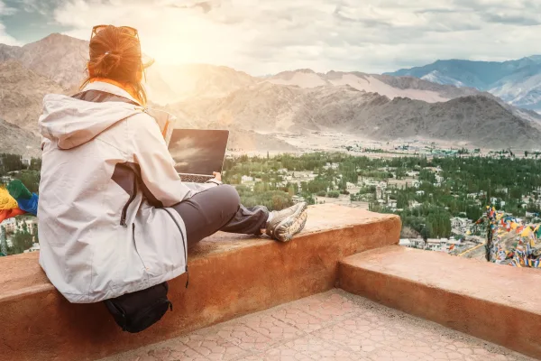 Femme en télétravail avec ordinateur portable face aux montagnes au coucher du soleil
