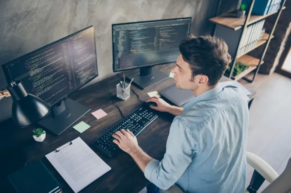 Développeur logiciel travaillant sur plusieurs écrans avec du code informatique