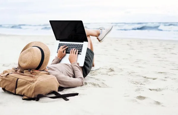 Nomade digital travaillant sur un ordinateur portable allongé sur une plage