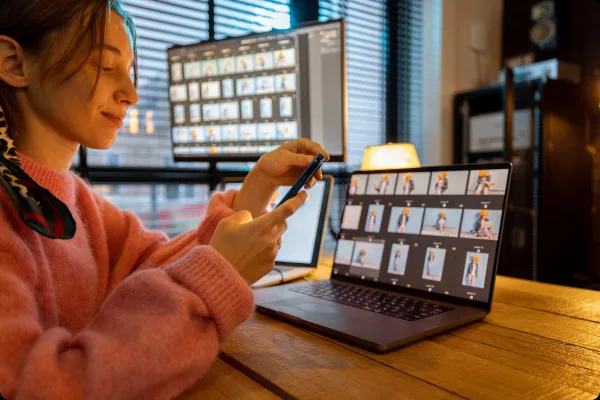 Créatrice de contenu gérant des photos sur smartphone et ordinateur portable dans un studio de création