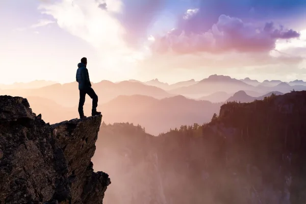 Homme au sommet d'une falaise contemplant l'horizon, symbole de confiance en soi, de courage et de réussite