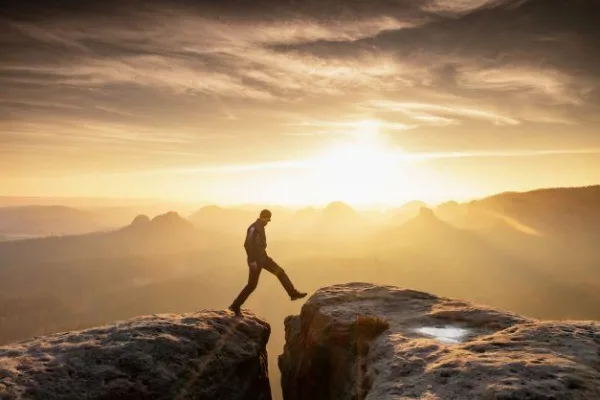 Homme franchissant un précipice en montagne, symbole de courage, de confiance en soi et de prise de décision