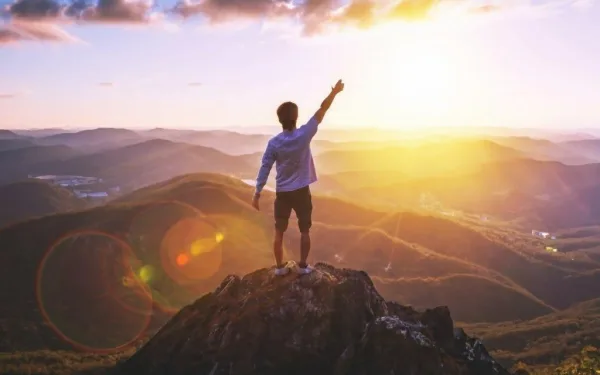 Homme au sommet d'une montagne pointant vers l'horizon, symbole de réussite et de vision