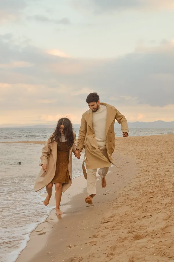 Père et fille courant main dans la main sur une plage au coucher du soleil