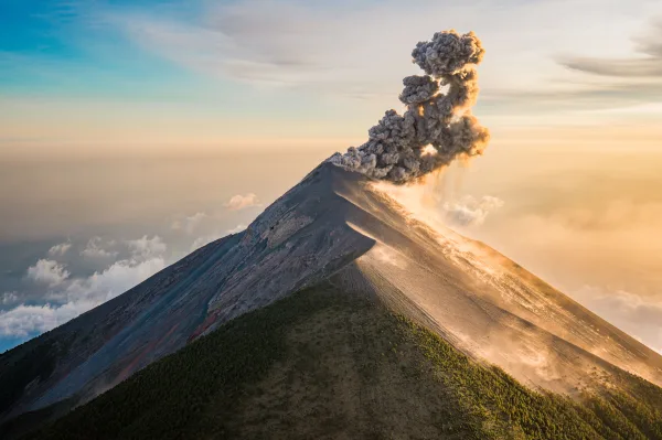 Volcan en éruption projetant un immense panache de cendres au lever du soleil