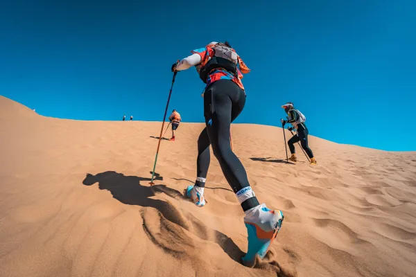 Randonneurs gravissant une dune de sable sous un ciel bleu éclatant